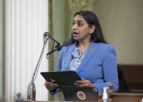 AD76 Patel Dr. Darshana Patel speaks from behind a podium with microphone in three quarter profile on the Assembly floor. The Assemblymember is visible from the waist up and holds an electronic tablet. She is wearing a periwinkle jacket with a floral blouse.