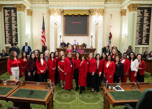 AD76 Patel A group photo of Legislative Women's Caucus members of the Assembly dressed in red attire photographed on the Assembly floor in front of the Speaker's dais. Dr. Darshana Patel, front row, fifth from right, wears a red pantsuit. American flag at left and California State Flag at right, flank the Speaker's dais